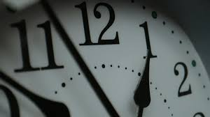 Close-up of an analog clock face near twelve and one, shallow depth of field, dim light